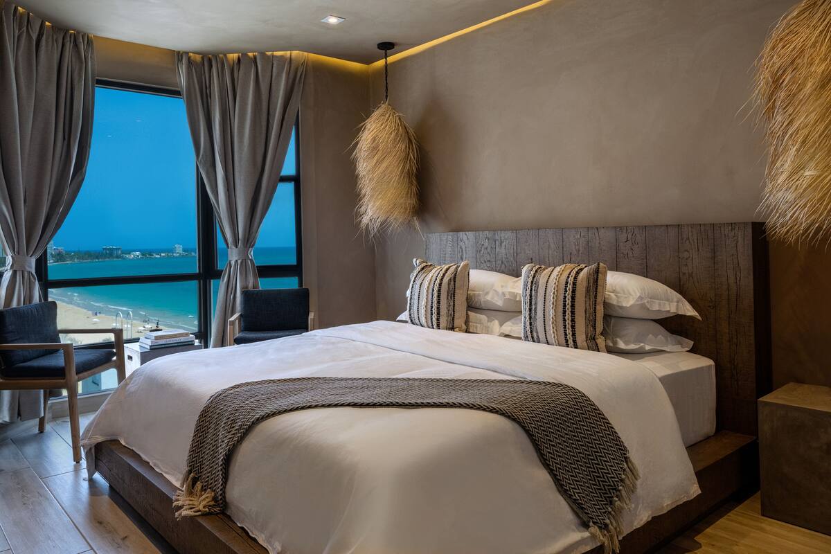 Une chambre d’hôtel moderne avec un grand lit, une vue sur la mer et une tête de lit en bois.