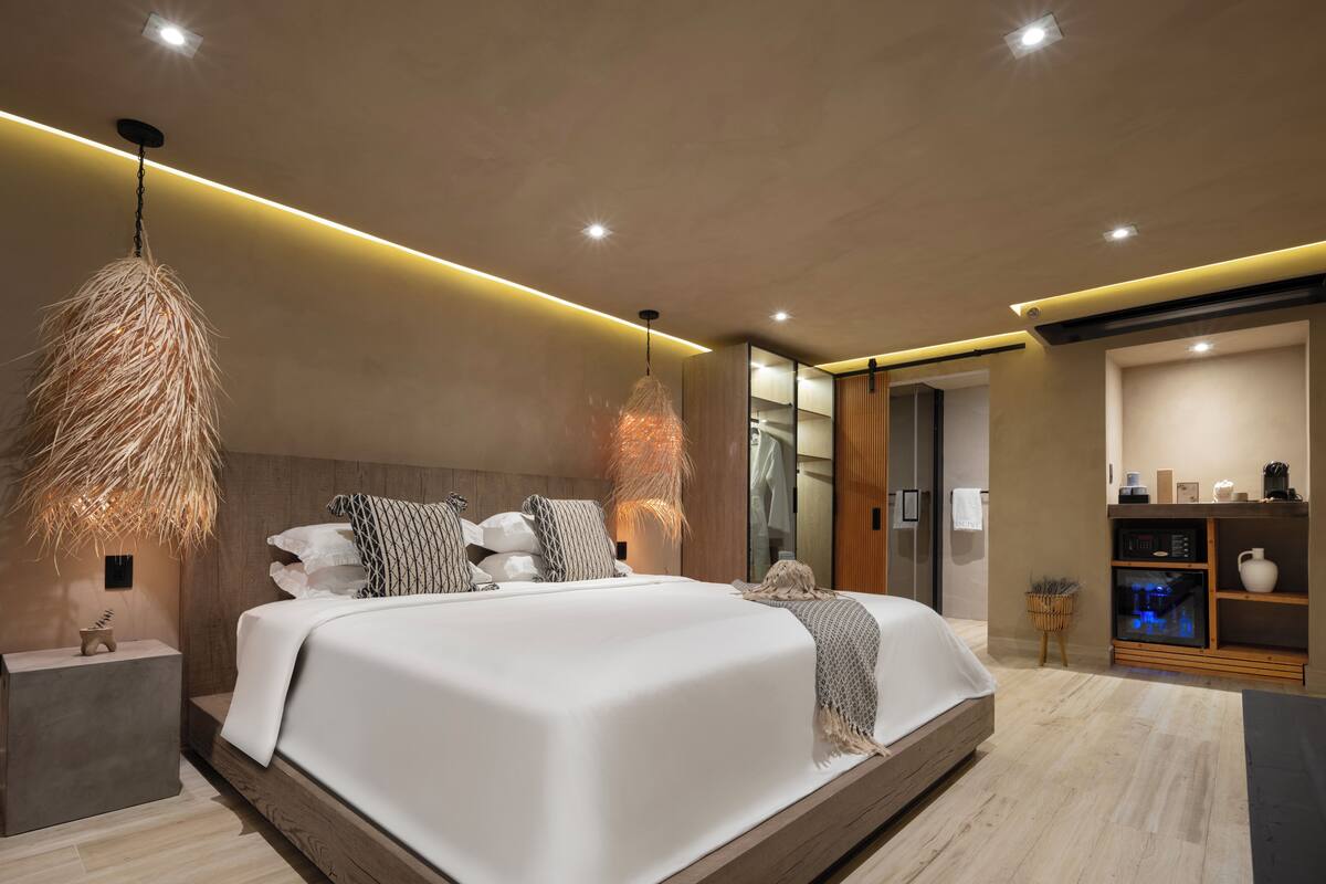 Une chambre moderne avec un grand lit, une tête de lit en bois et un luminaire suspendu.