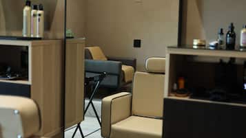 Un salon moderne au design minimaliste, avec un espace salon central comprenant un canapé et des fauteuils, ainsi qu'un comptoir où sont exposés divers produits capillaires.