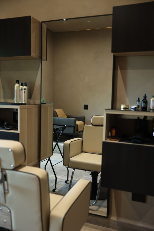 Un salón moderno con diseño minimalista, que presenta una zona de estar central con un sofá y sillones, y una barra con diversos productos para el cabello.
