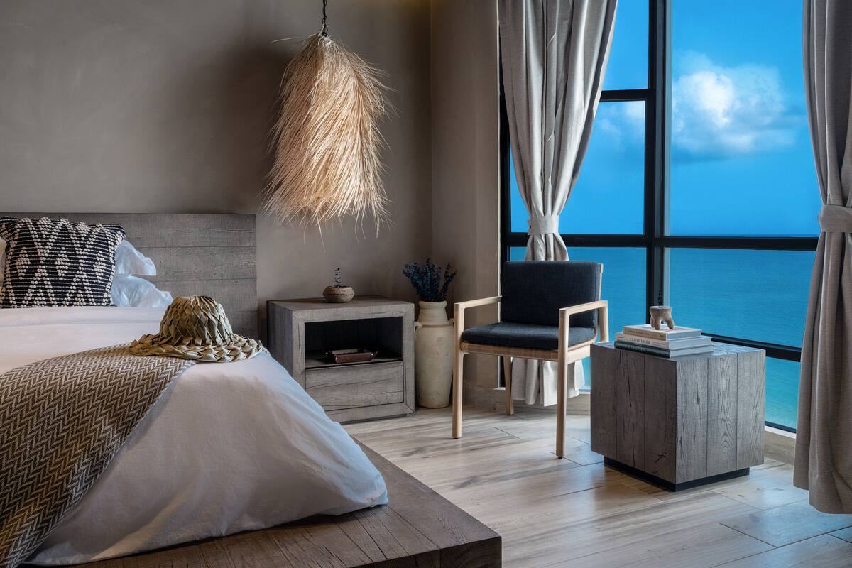 Une chambre à coucher moderne avec un grand lit, une table de chevet, une chaise et une vue sur l’océan.