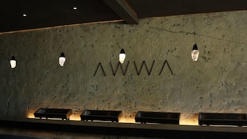 Una zona de bar con pared texturizada, iluminación colgante y taburetes negros.