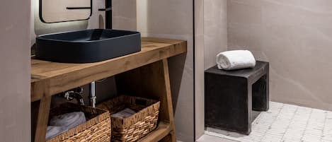 A modern bathroom with a round black sink, a mirror, and a shower area.