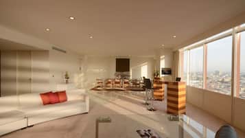 A spacious living room with a glass coffee table, a white sofa with red cushions, a wooden side table, and a city view through large windows.