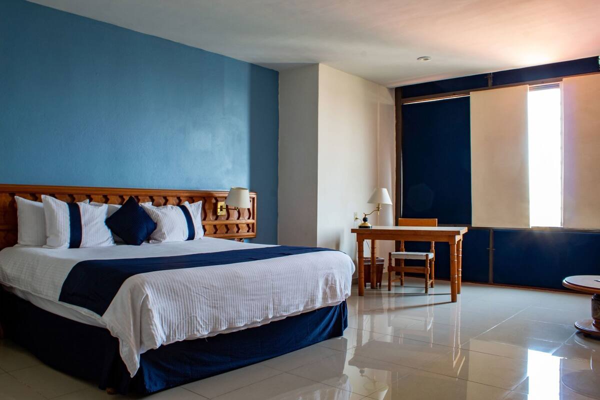 A hotel room with a large bed, a desk, and a chair.