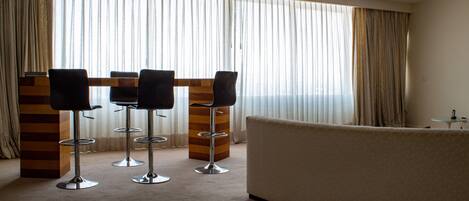 Una habitación de hotel moderna con un ventanal grande, un sofá y tres taburetes de bar.