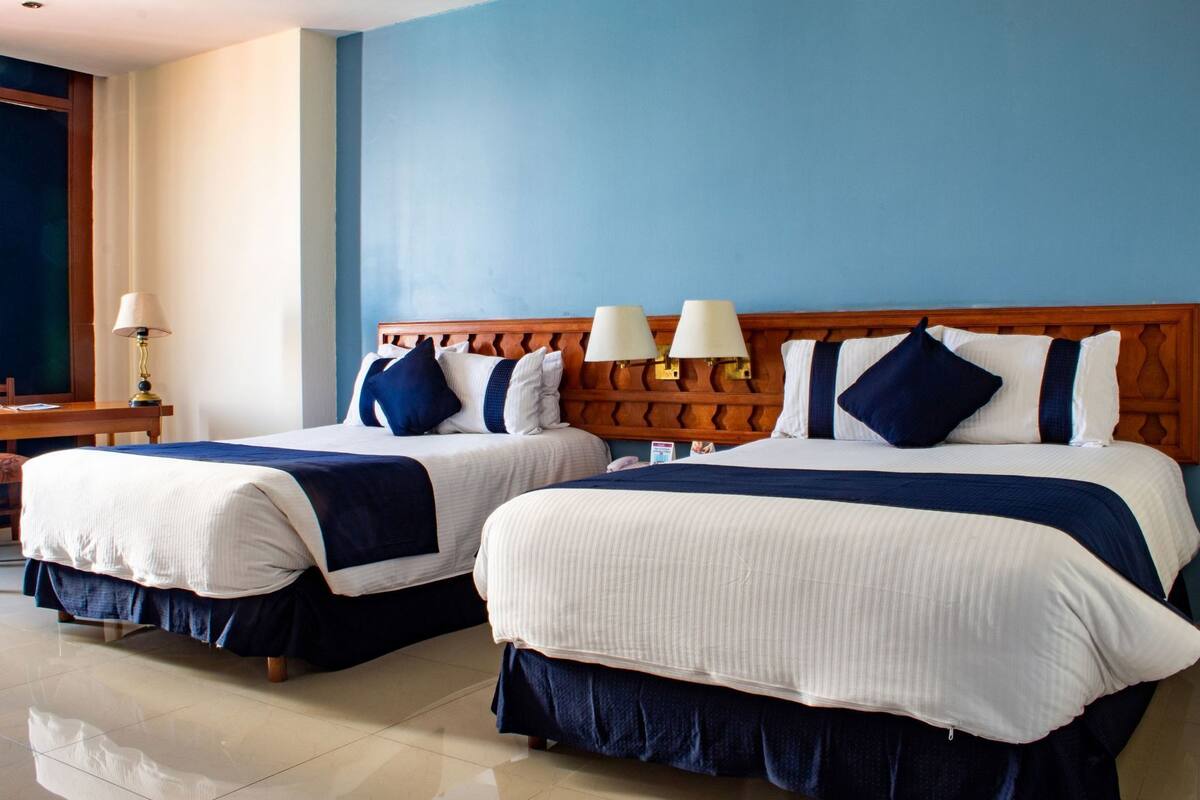 Two double beds with matching headboards, bedside lamps, and a wooden nightstand with a lamp.