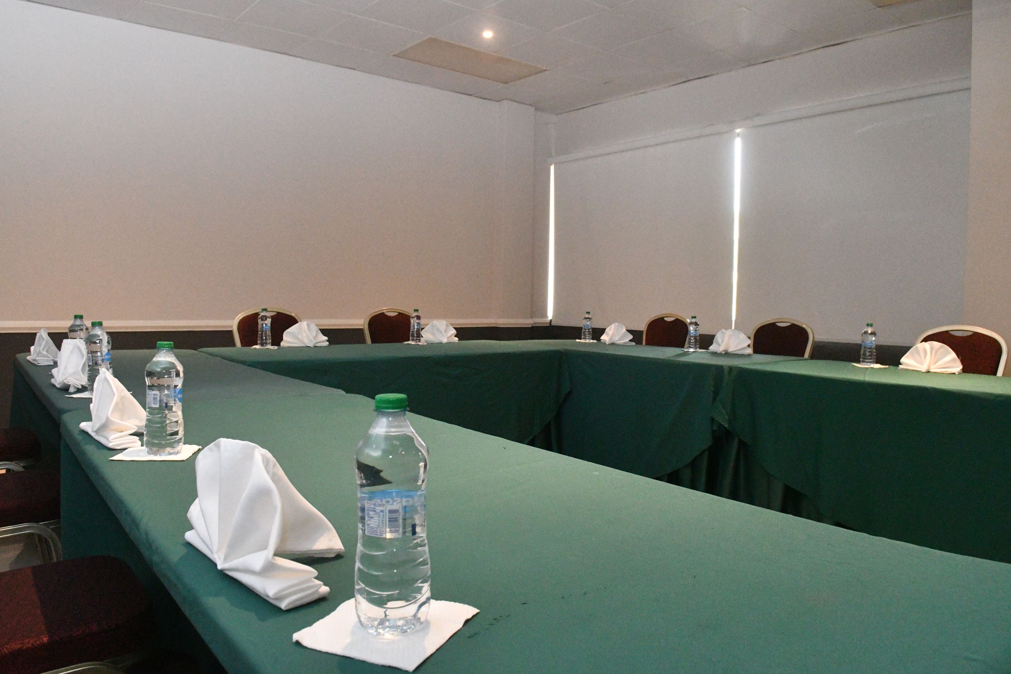 Un salón de conferencias con una larga mesa dispuesta para una reunión, equipado con botellas de agua y servilletas blancas dobladas.
