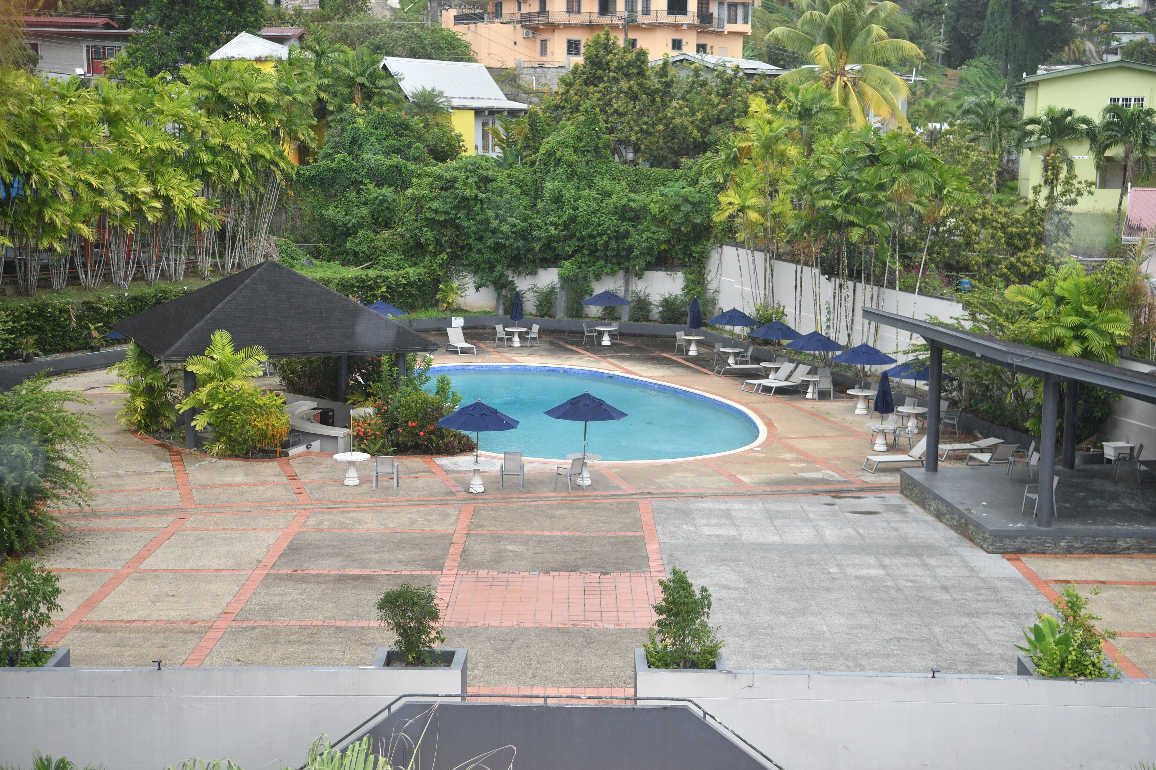 A pool area with lounge chairs and umbrellas, surrounded by palm trees and a brick pathway.