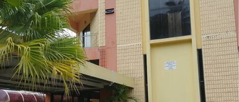 A multi-story building with a yellow facade, a covered entrance area with potted plants, and a parked car.