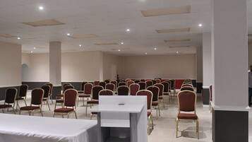 Un salón de conferencias con filas de sillas rojas, una mesa blanca y un atril.