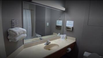 Un baño con lavamanos, espejo, toallero y retrete.
