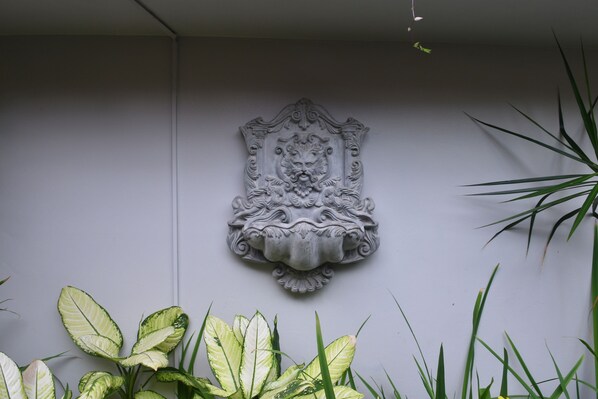 Un escudo decorativo montado en la pared, con diseños intrincados, rodeado de plantas verdes.