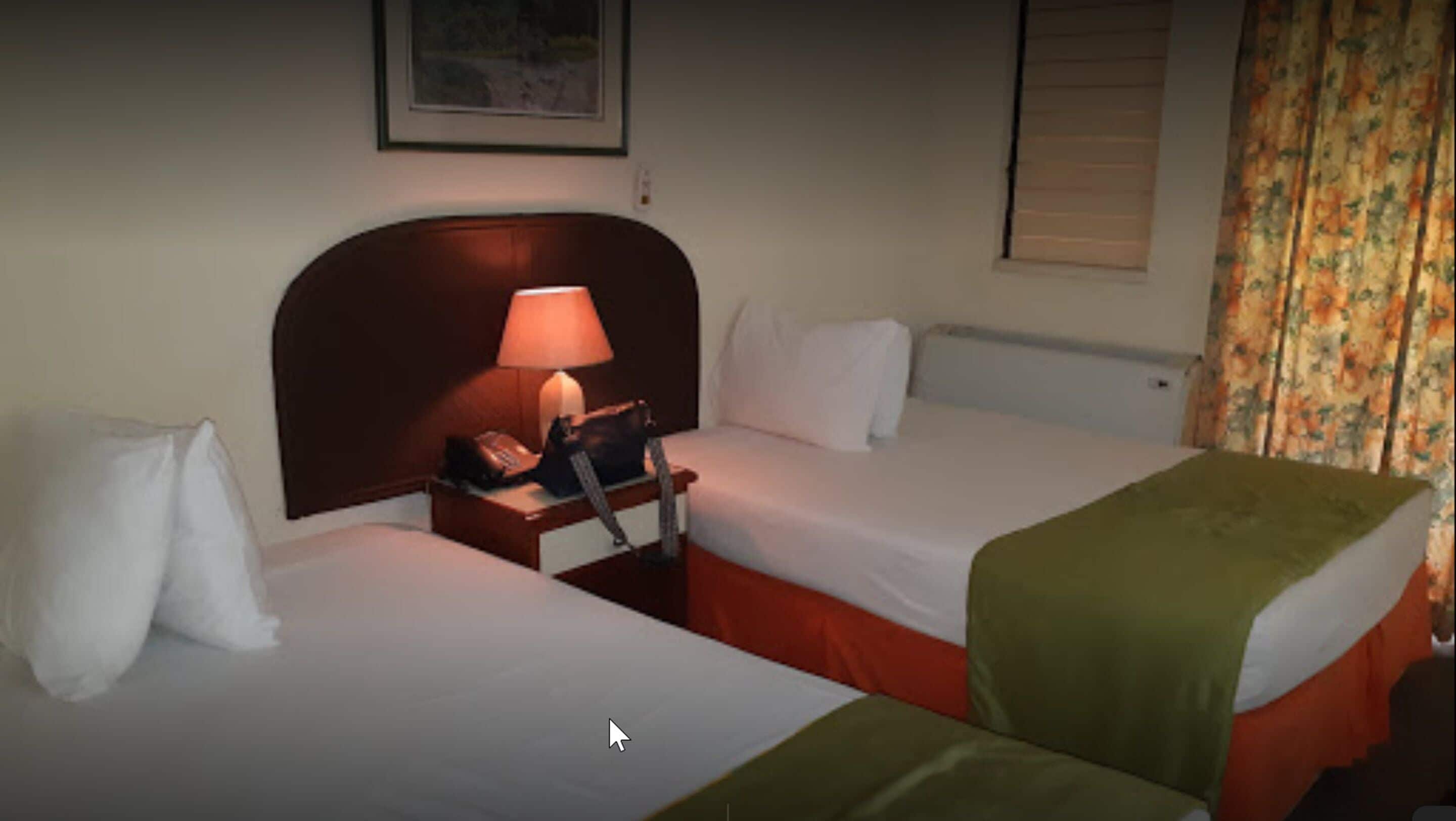 A hotel room with two single beds, a nightstand with a lamp, and a window with curtains.