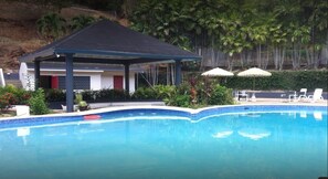 Relax by the serene pool surrounded by lush greenery and a shaded pavilion.