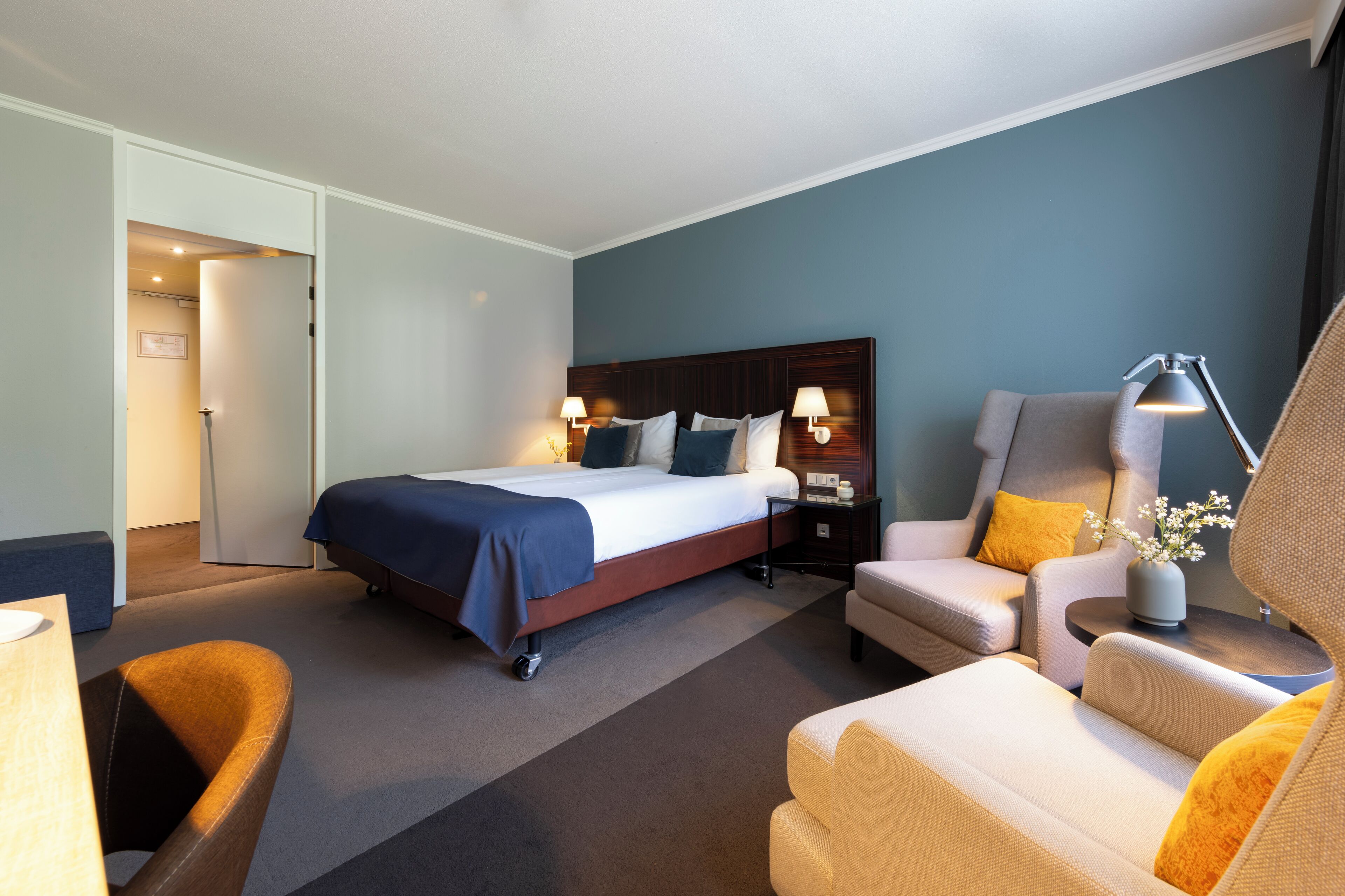 A hotel room with a bed, two bedside tables with lamps, a sofa, and a chair.