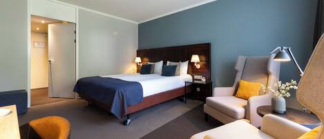 A hotel room with a bed, two bedside tables with lamps, a sofa, and a chair.