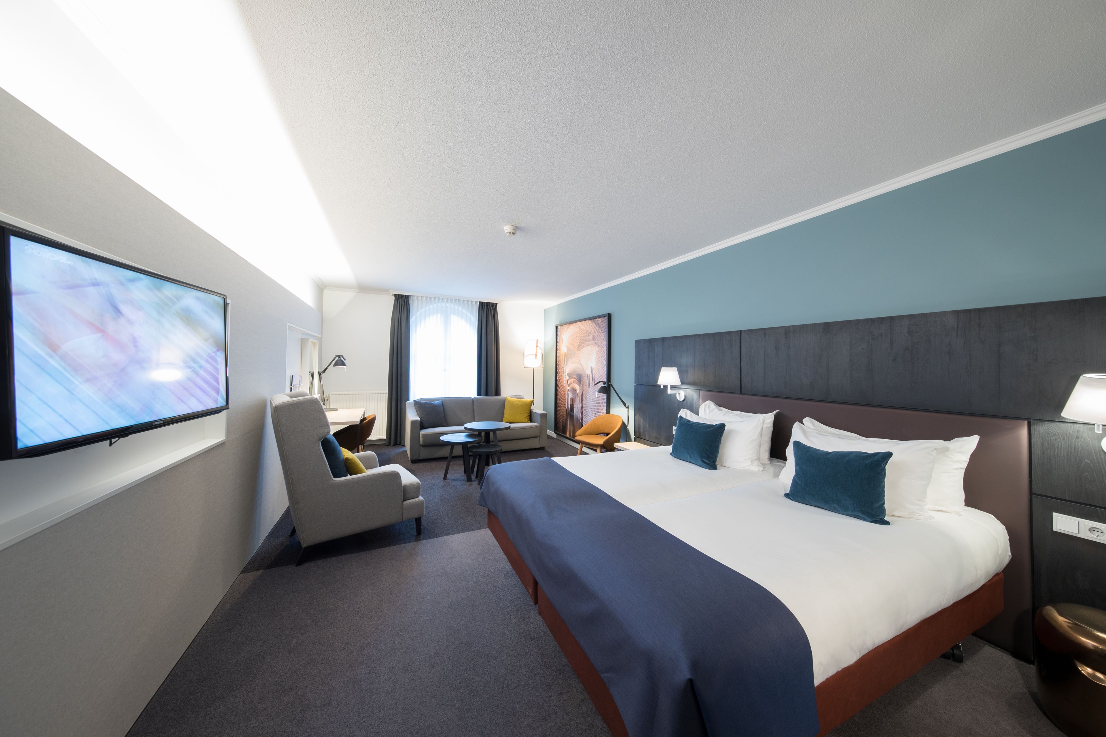 A hotel room with a large bed, a flat-screen TV, a sofa, a small table, and a desk.