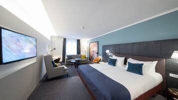 A hotel room with a large bed, a flat-screen TV, a sofa, a small table, and a desk.