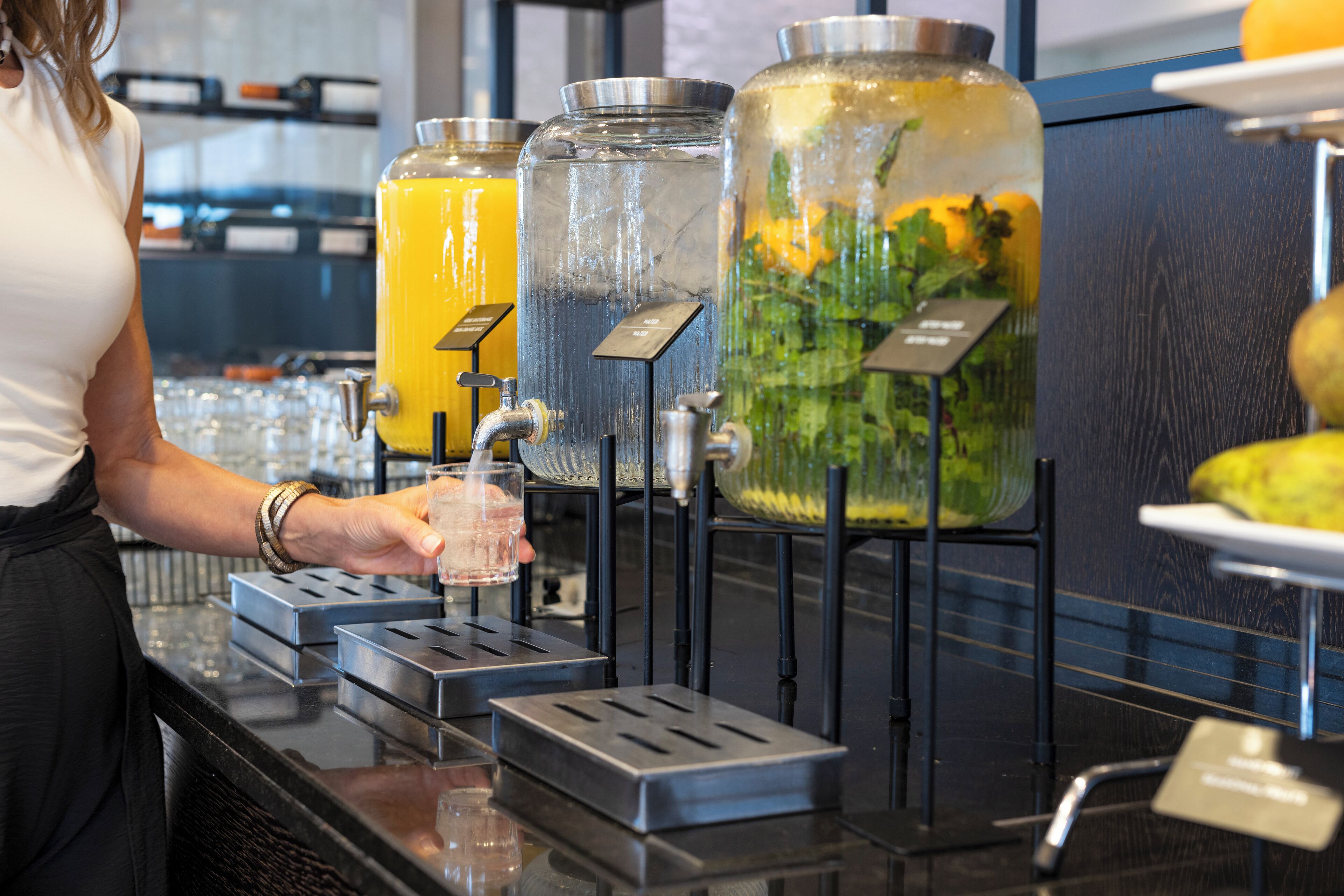 Eine Getränkespenderstation mit verschiedenen Optionen, darunter ein klares Glas und ein Glas mit gelber Flüssigkeit.