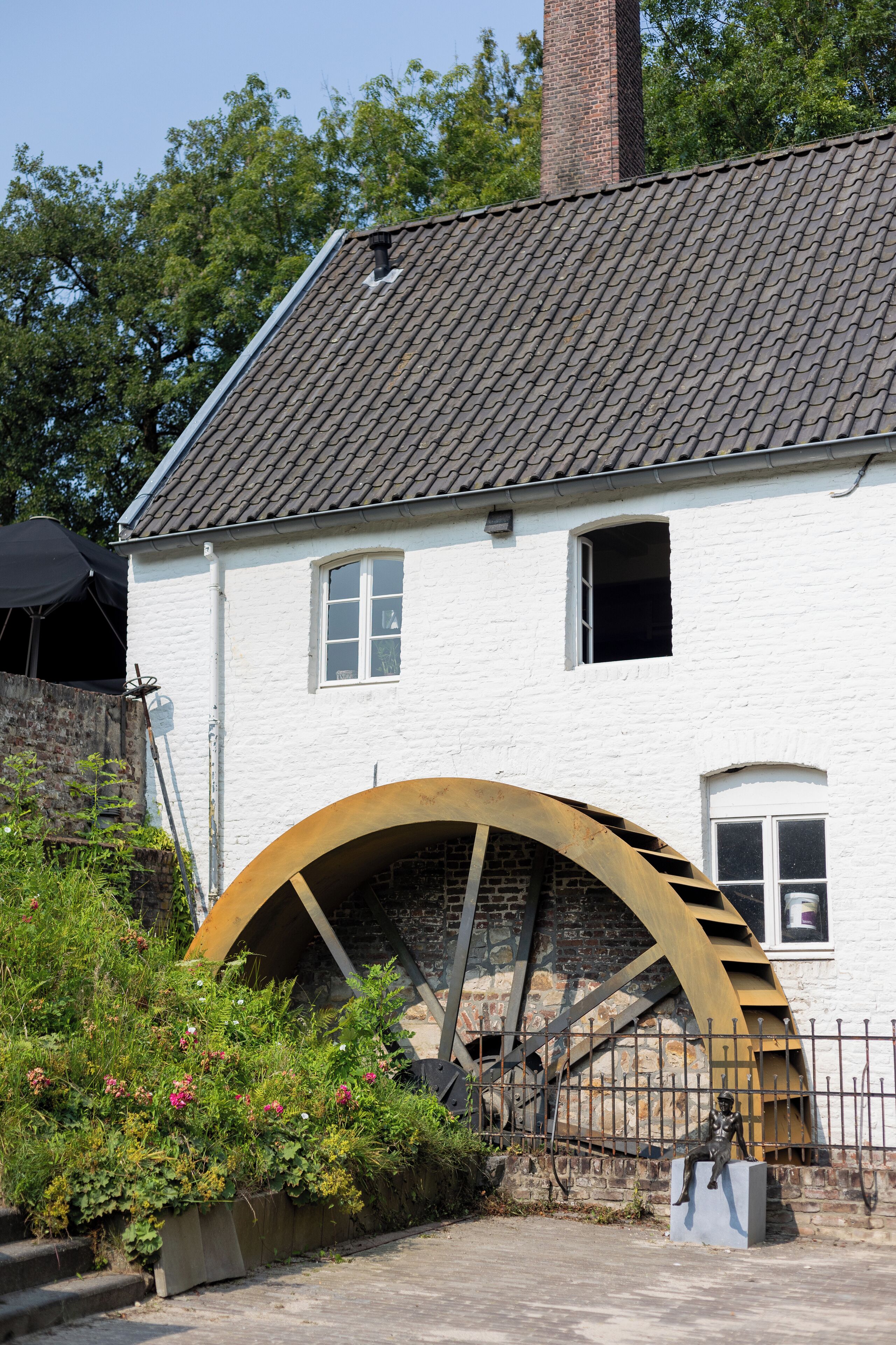 A white building with a large water wheel, a window, and a chimney.