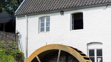 Een wit gebouw met een groot waterrad, een raam en een schoorsteen.