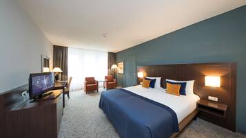 Une chambre d’hôtel avec un grand lit, un bureau avec un ordinateur, deux chaises et un téléviseur.