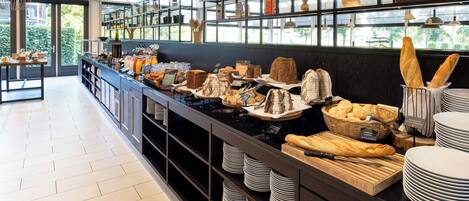 A buffet area with various food items, including bread and pastries, arranged on a counter with plates and serving utensils.