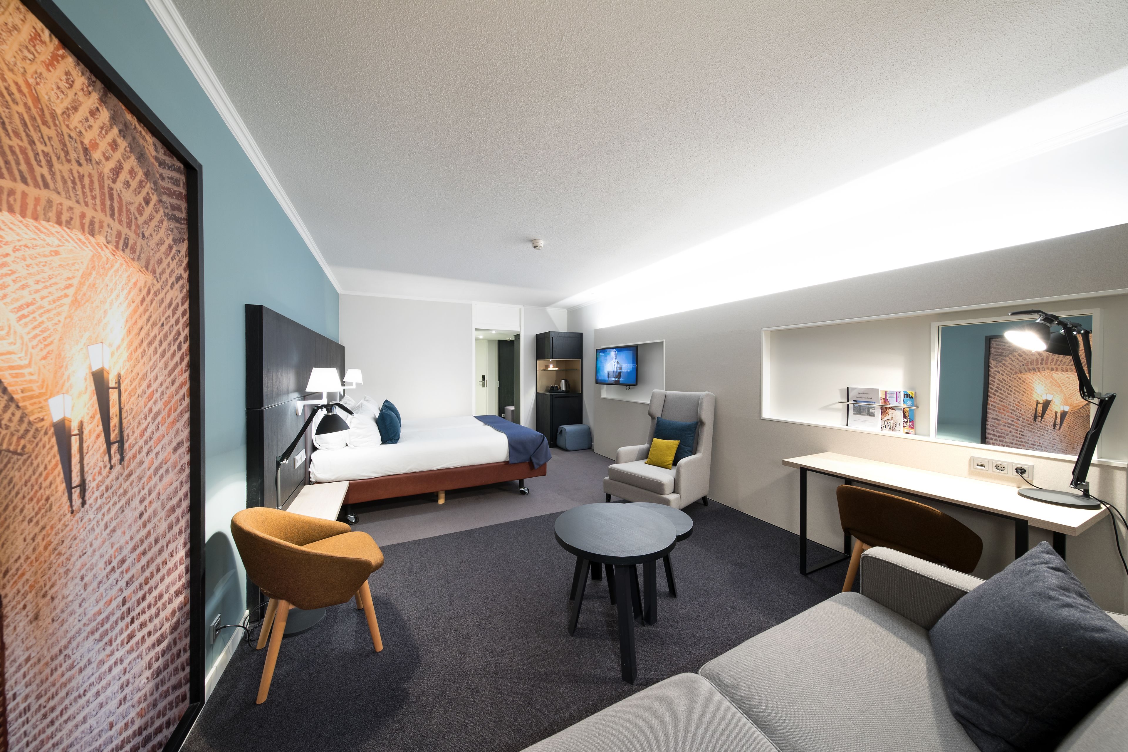 Een moderne hotelkamer met een bed, een bureau, een bank, een stoel en een televisie.