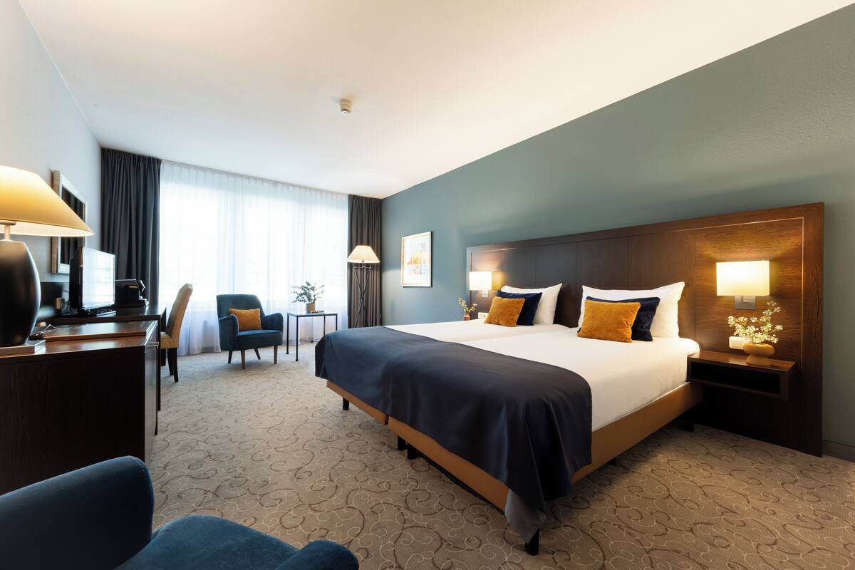 Een hotelkamer met een groot bed, een bureau, een stoel en een kleine tafel met een lamp.