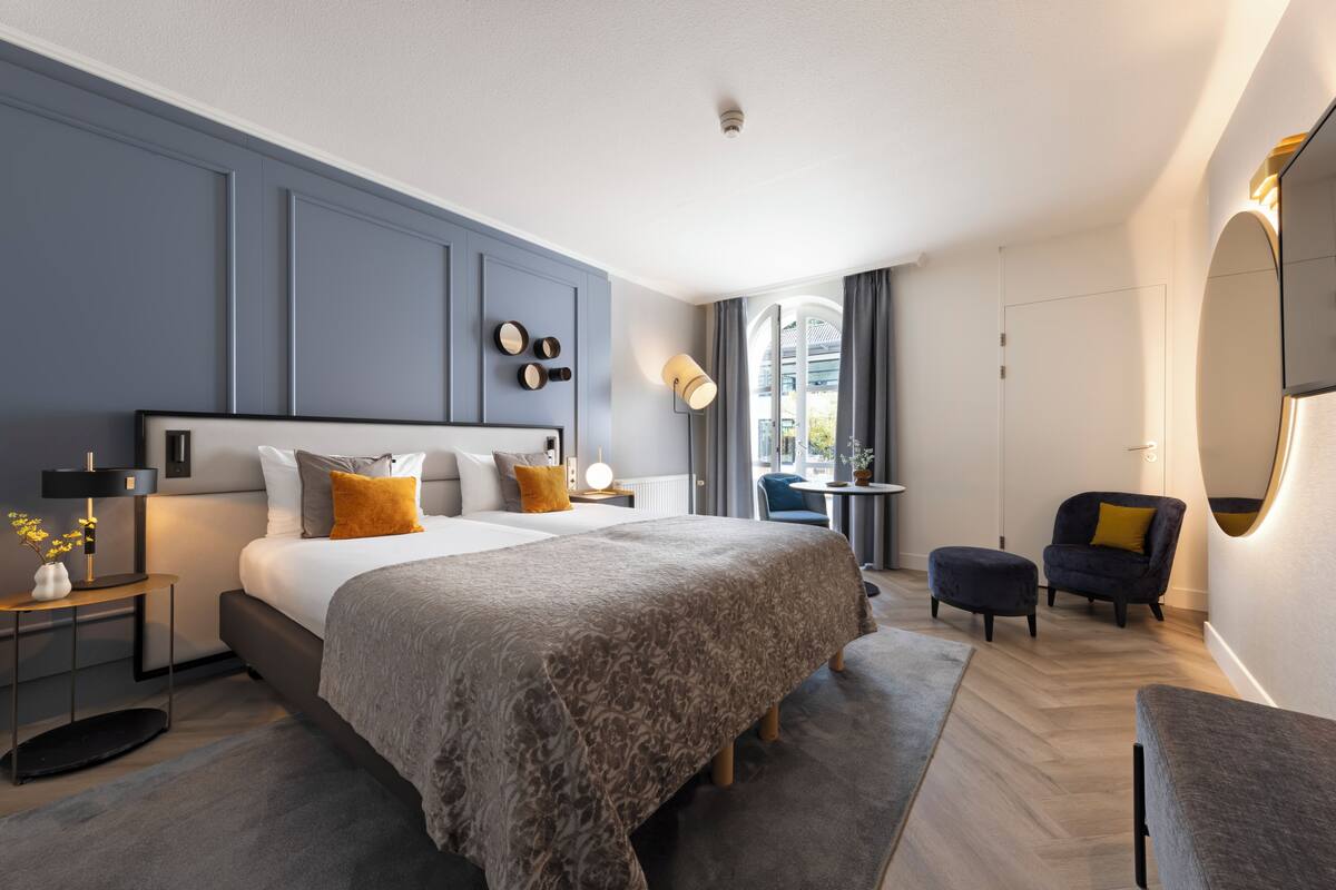 Een moderne slaapkamer met een groot bed, nachtkastjes, een stoel en een klein tafeltje.