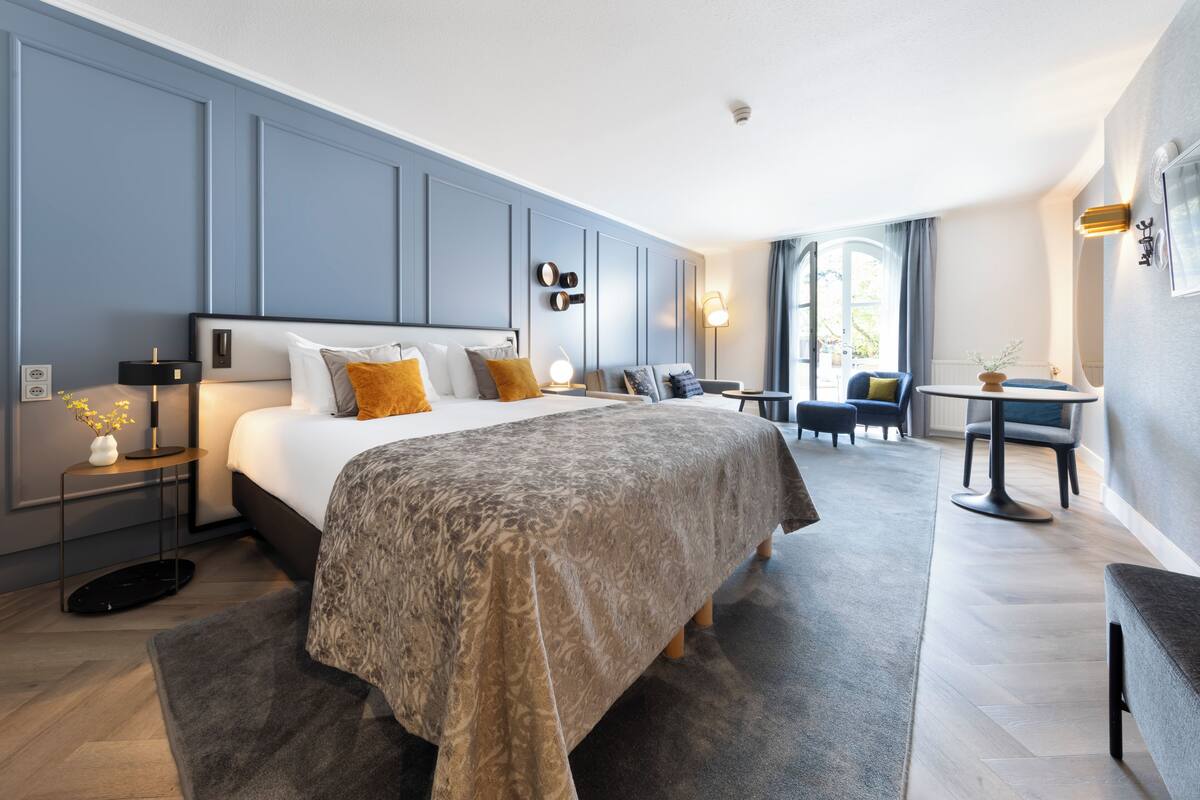 Een moderne hotelkamer met een groot bed, nachtkastjes, een bureau en uitzicht op het groen.
