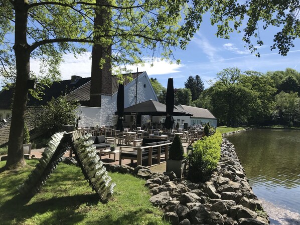 A riverside restaurant with outdoor seating, stone walls, and a view of the water.