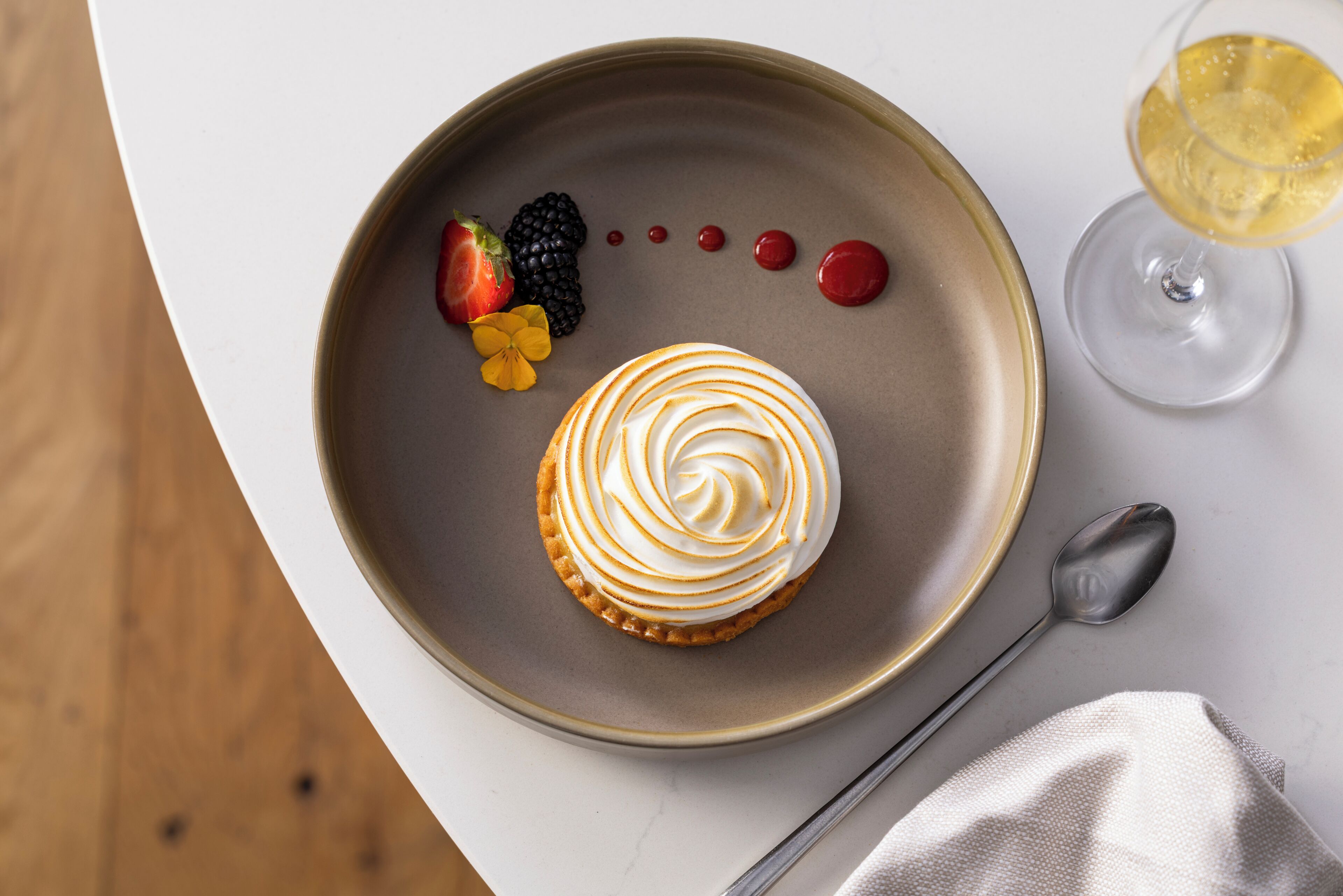 A dessert plate with a pastry, berries, and a glass of a yellow beverage on a table.