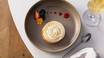 A dessert plate with a pastry, berries, and a glass of a yellow beverage on a table.