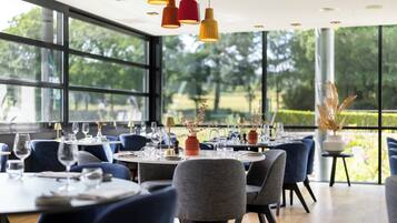 Een restaurant met ronde tafels, blauwe stoelen en hangende lampen.