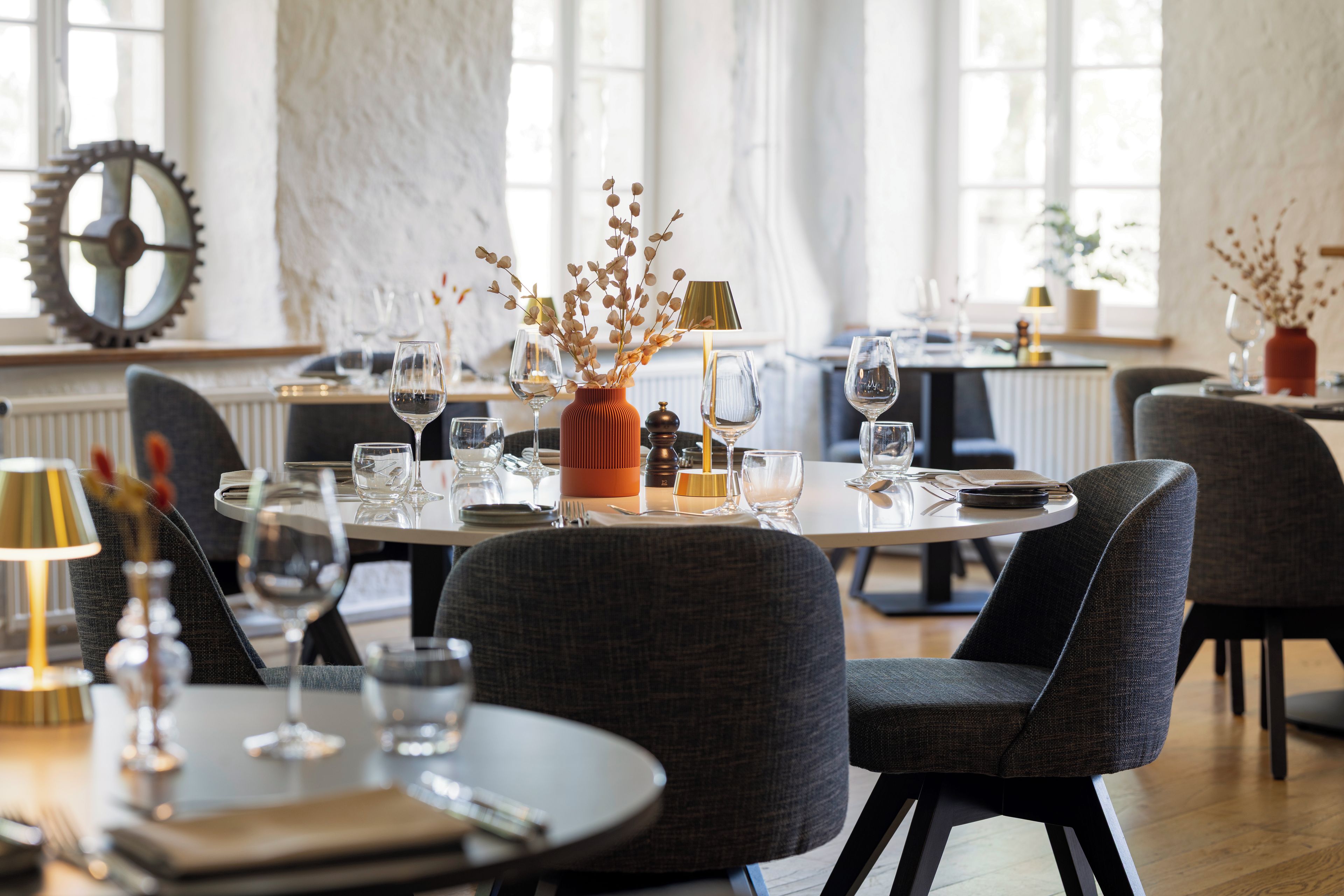 A dining area with round tables, chairs, and a variety of tableware including wine glasses and plates.