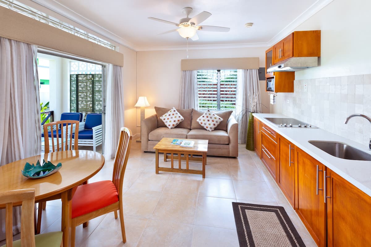 A compact living space with a kitchenette, a sofa, a dining area with a table and chairs, and a view through a window with curtains.