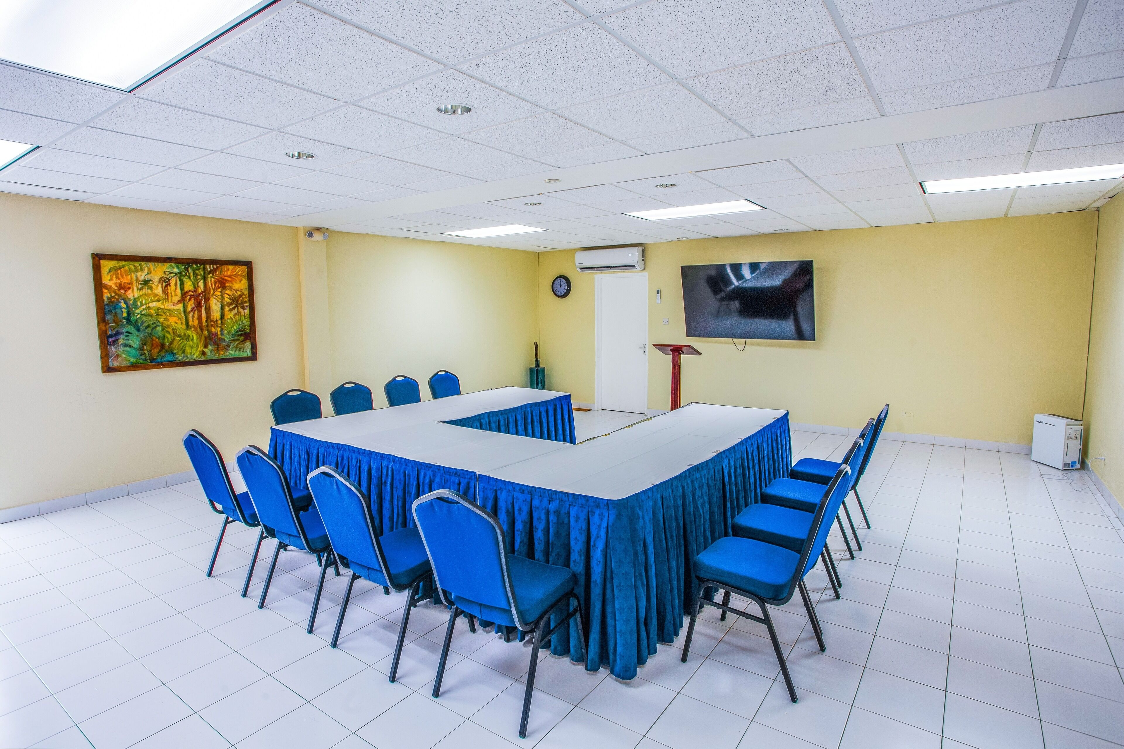 A conference room with a large table, blue chairs, a clock, and a television on the wall.