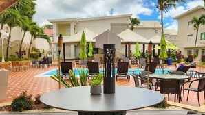 Zona de piscina al aire libre con sillones de descanso y sombrillas, rodeada de palmeras y un cielo despejado.