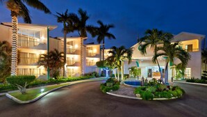 Un hotel de varios pisos con piscina, palmeras y una entrada bien iluminada.