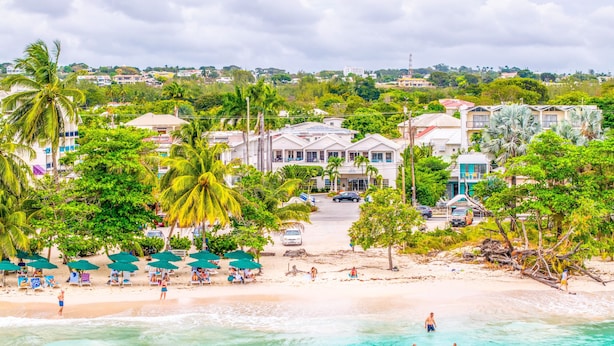 Un hotel frente a la playa con edificios de varios pisos, palmeras y una playa de arena.