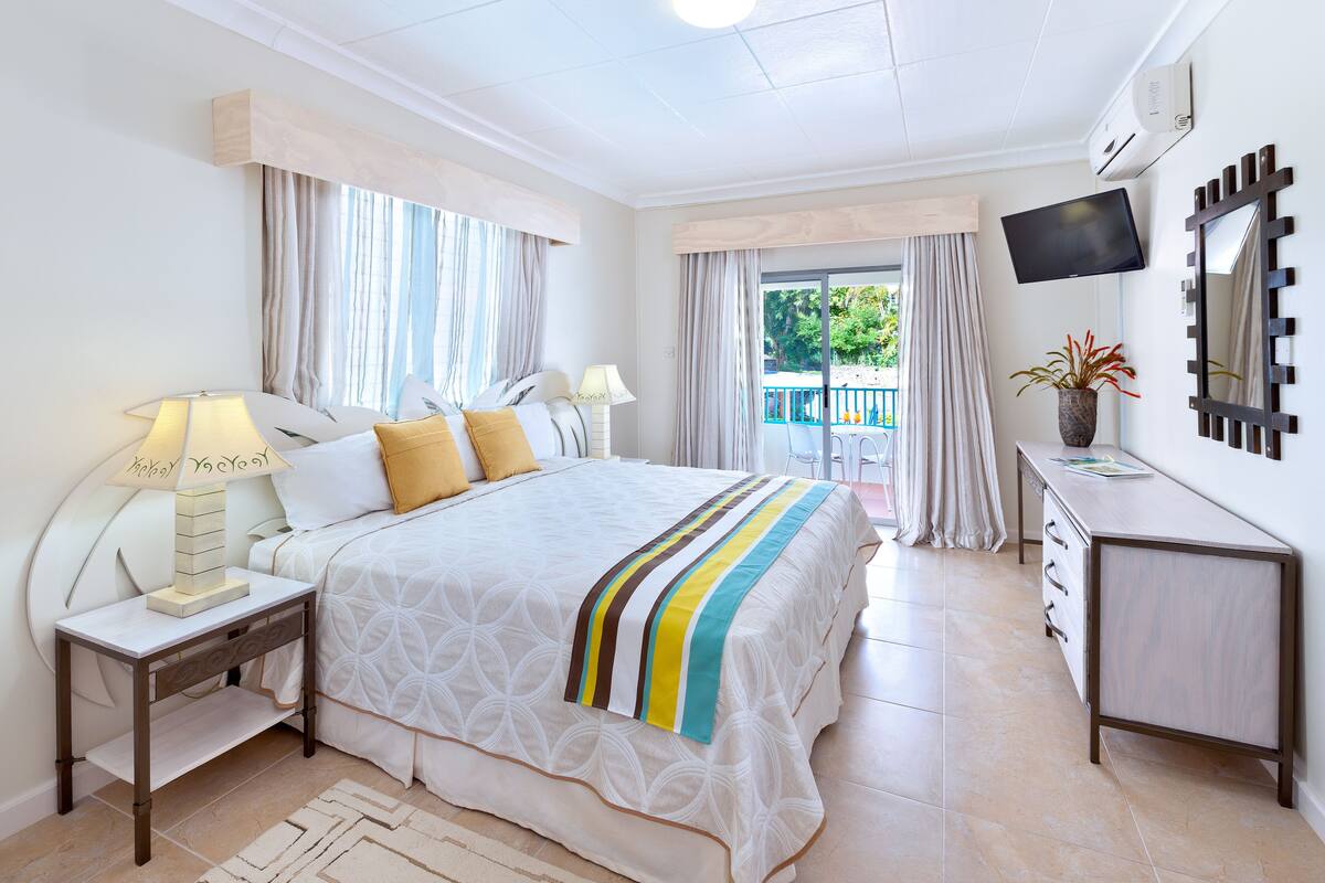 A hotel room with a bed, bedside tables, a TV, a dresser, and a balcony with curtains.