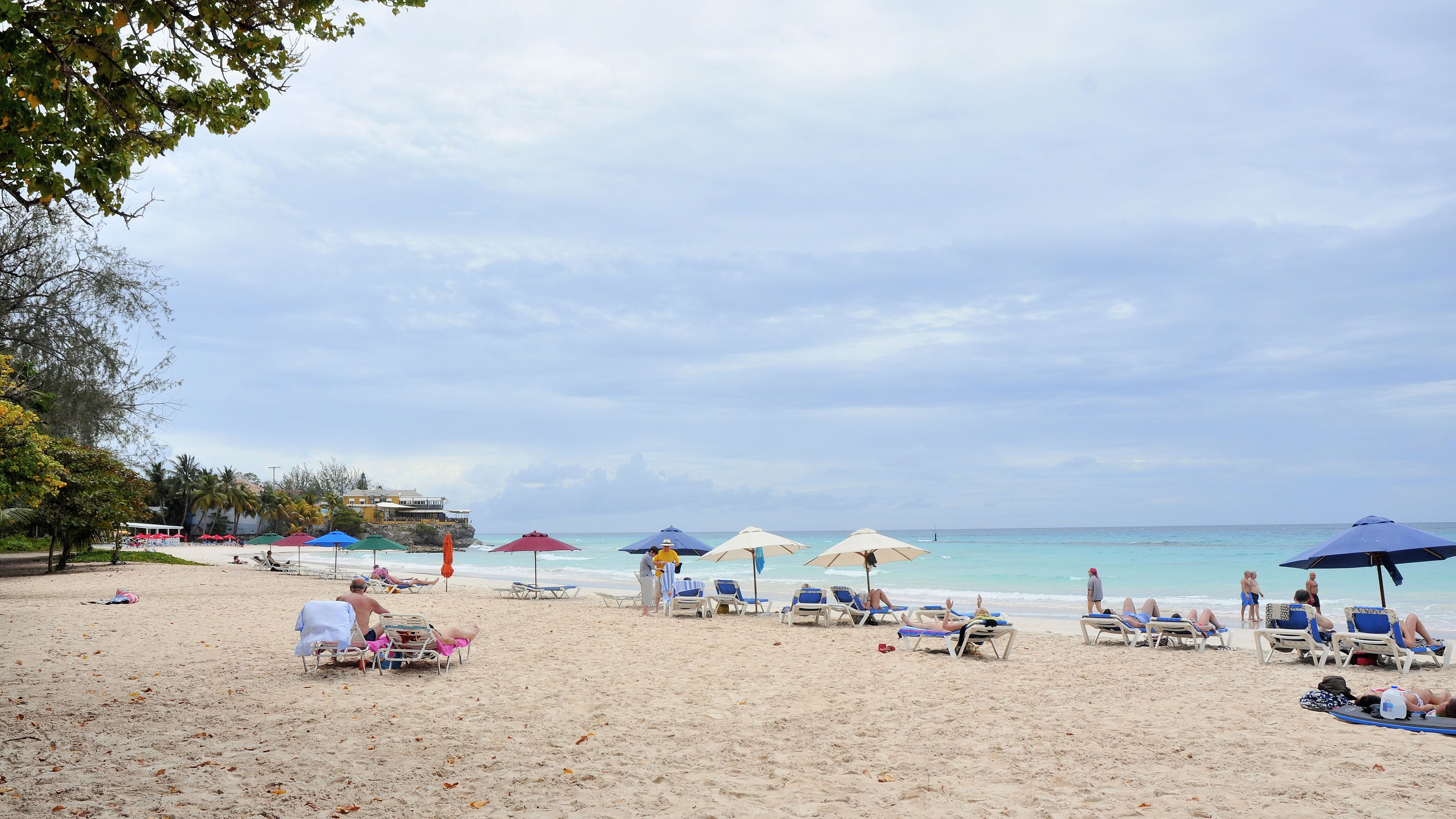 A beach with sun loungers and umbrellas, a clear sky, and a building in the background.