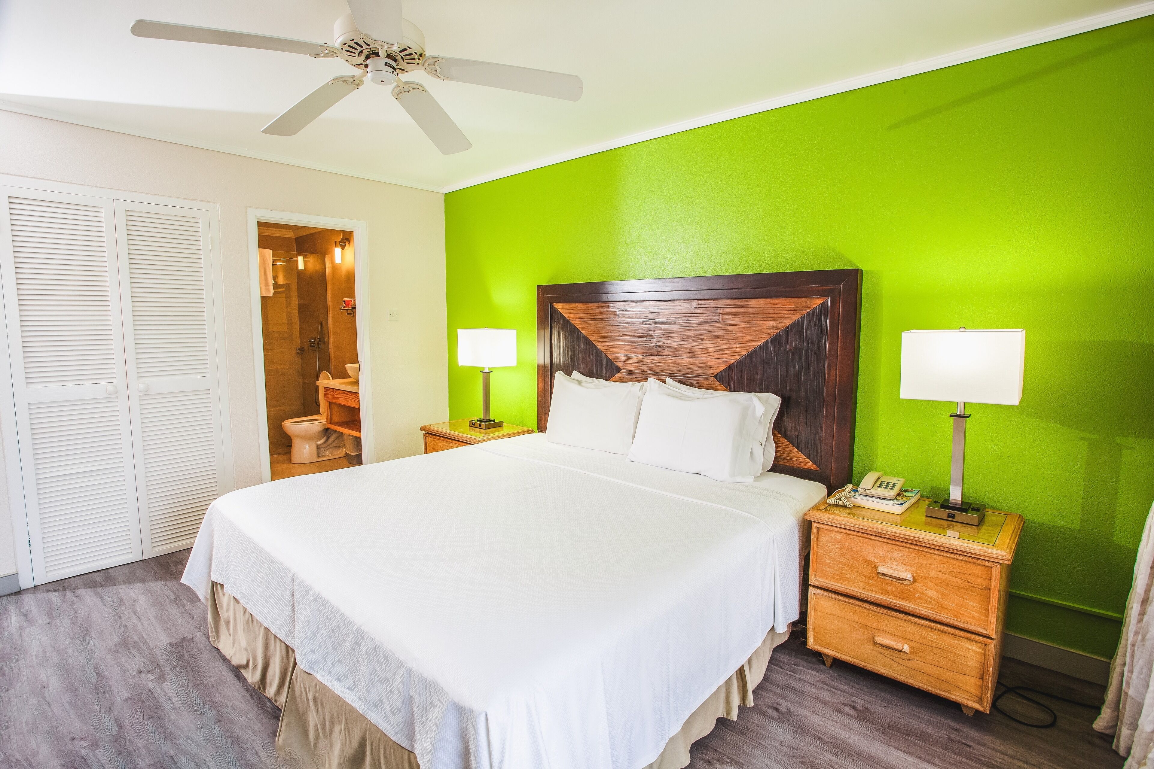 A hotel room with a large bed, two bedside tables with lamps, a wooden headboard, and a ceiling fan.