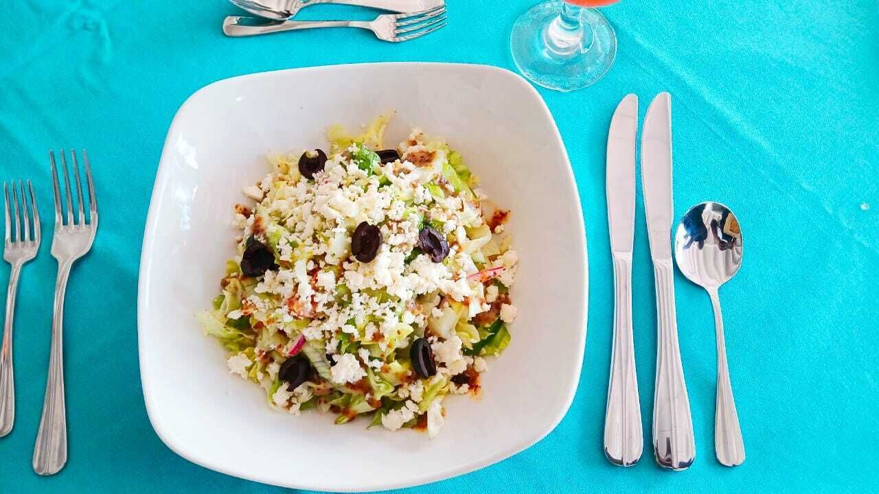 A white plate with a salad on a turquoise tablecloth.