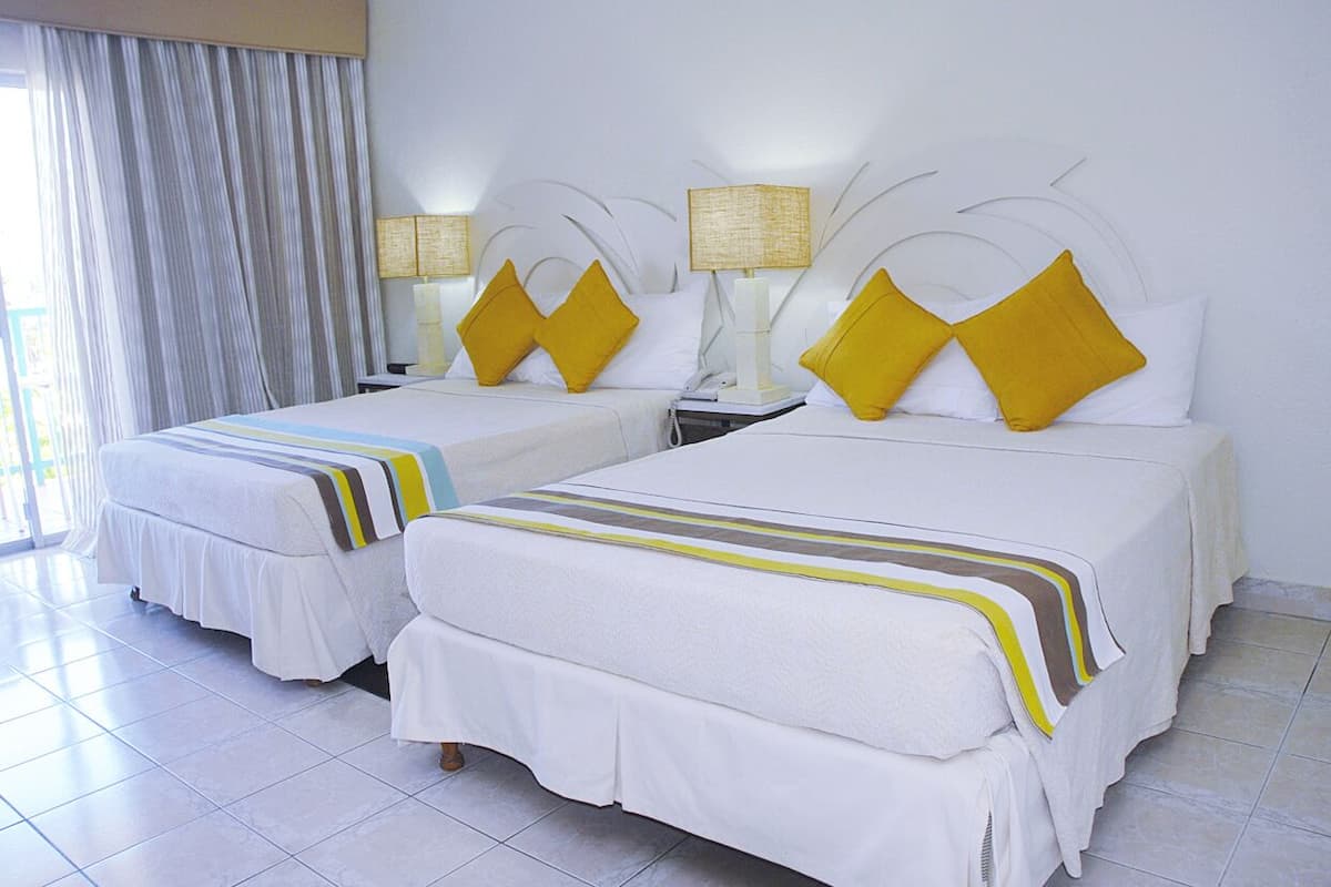 A hotel room with two beds, each with white bedding and yellow pillows, and a large window with white curtains.