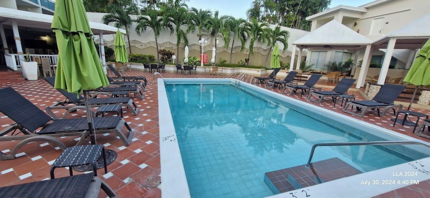 A pool area with lounge chairs and umbrellas, surrounded by a tiled deck and palm trees.