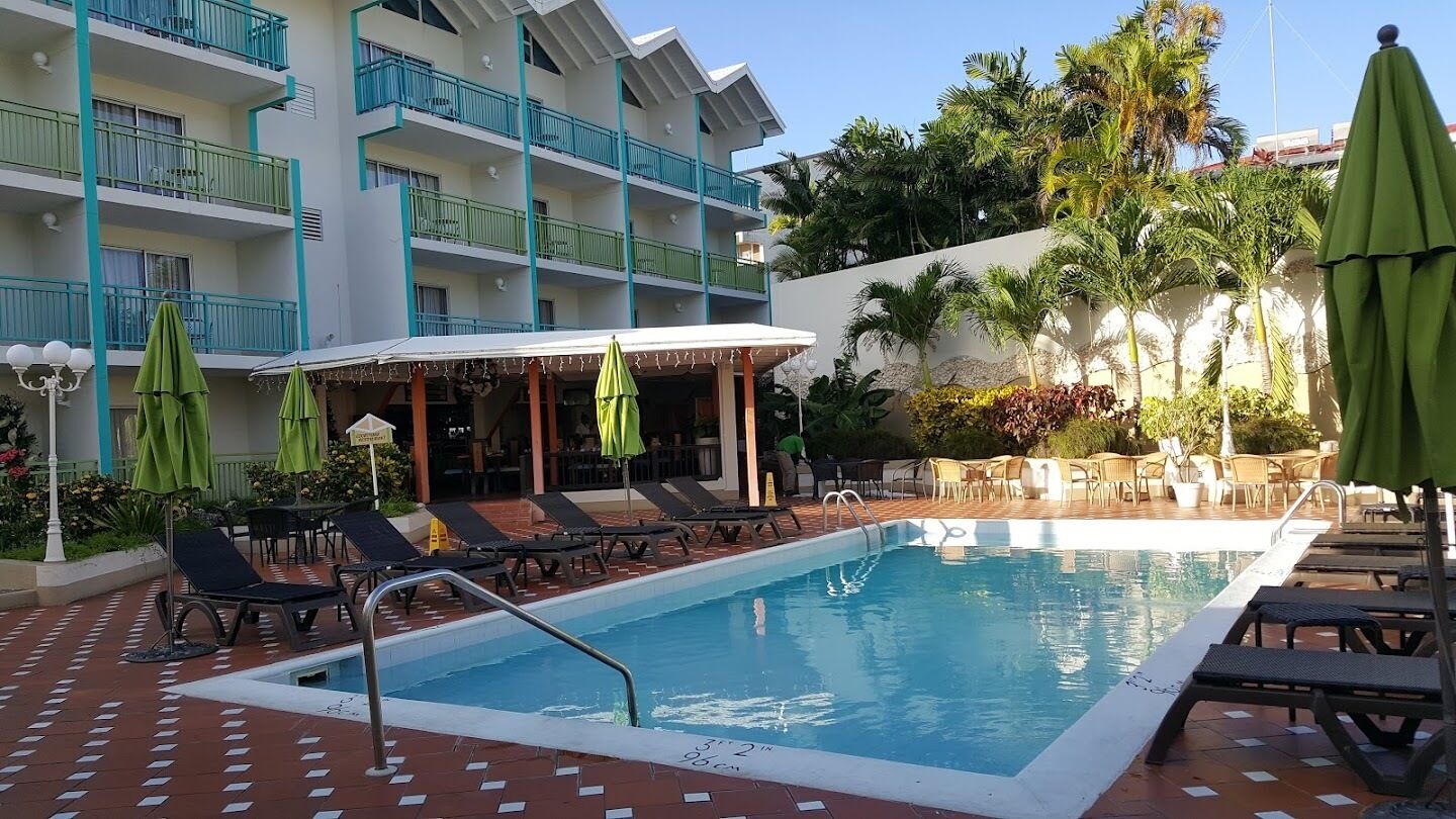 A swimming pool with lounge chairs and umbrellas, surrounded by a multi-story building with balconies.