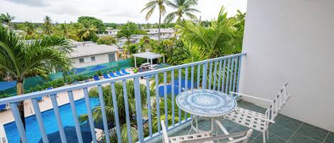 Un balcón con vista a una piscina, palmeras y un pequeño conjunto de mesa y sillas.